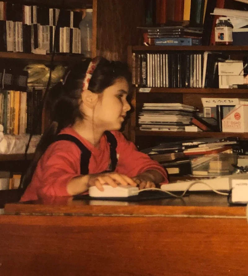 Noemi as a child typing on a keyboard in a book-lined study